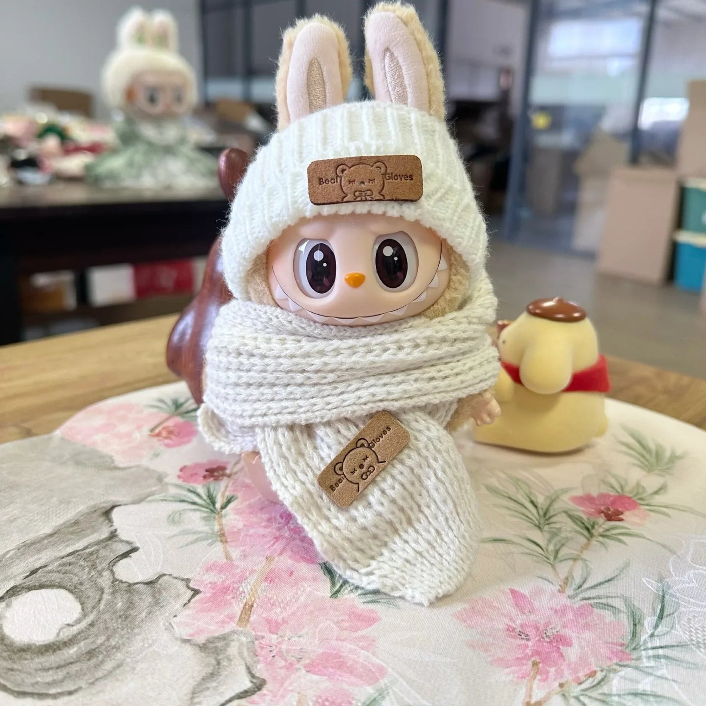 Knit Beanie on 17cm plush doll: cream-white cable-knit beanie with bear patch, pink-and-cream checkered knit scarf with be...