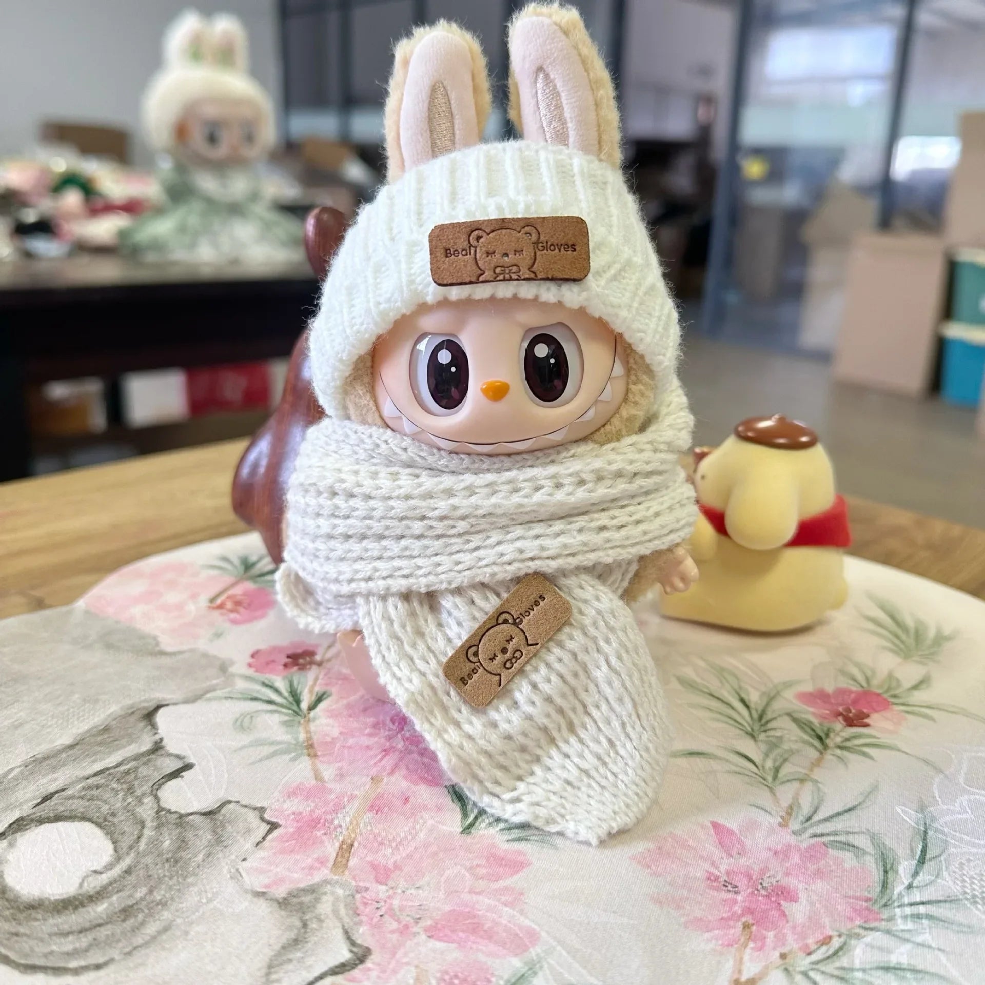 Knit Beanie on 17cm plush doll: cream-white cable-knit beanie with bear patch, pink-and-cream checkered knit scarf with be...